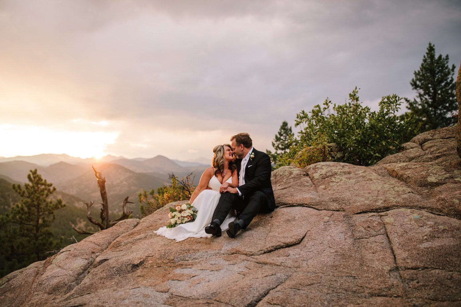 Bride and groom cuddling on mountain side at sunset