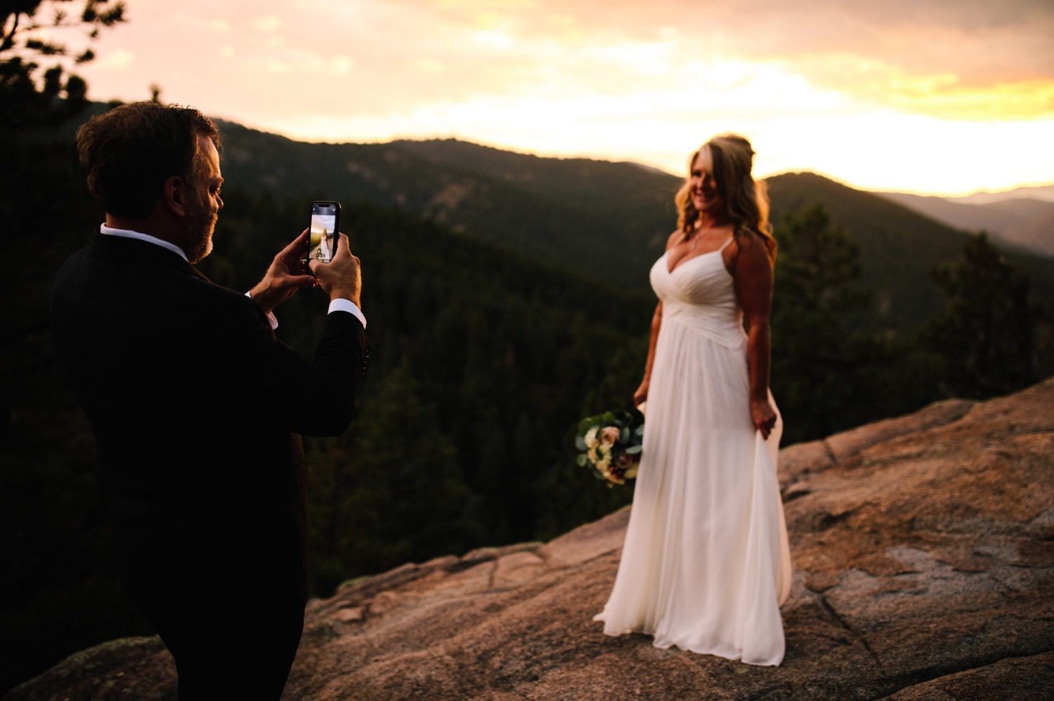 Groom taking a photo of his bride at sunset